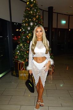 a woman standing in front of a christmas tree wearing a white skirt and crop top