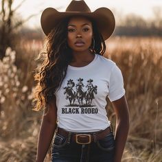 Dive into the essence of Western elegance with our 'Black Rodeo Unisex Tee,' a fashion statement that celebrates heritage and the adventurous spirit of three stunning Black women on their majestic rides. Perfect for individuals passionate about Western equestrian culture, heartland melodies, and the vibrant traditions of rodeo, this tee is a tribute to the enduring strength of cowgirl legends. Crafted from premium soft materials for ultimate comfort and durability, it's ideal for any setting, from country outings to casual gatherings. Offering a range of sizes to ensure a perfect fit for everyone, this versatile tee bridges modern fashion with traditional homage, making it a must-have for those who cherish the legacy of Black cowgirls and the timeless charm of Western culture, all while em Cattle Barons Ball Outfit, Women Cowboy Outfits, Cowgirl Outfits Black Women Rodeo, Country Outfit Black Women, Band Merch Tops With Custom Print, Fitted Band Merch Shirt, Black Cowgirl Outfits For Women, Cali Cowgirl, Black Rodeo Outfits For Women