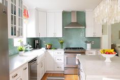 a kitchen with white cabinets and green backsplashing on the walls, along with stainless steel appliances