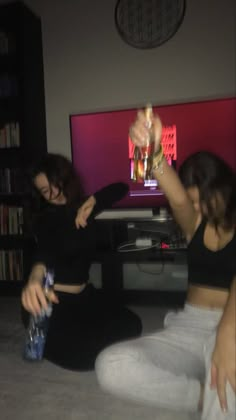 two women are sitting on the floor playing video games in front of a flat screen tv