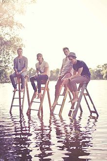 four men are sitting on stools in the water while one man is standing up