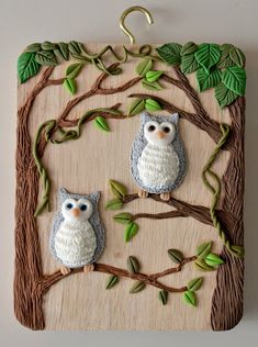 two owls sitting on a tree branch with green leaves in the shape of an ornament