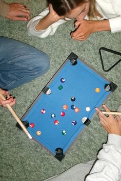 two people sitting on the floor playing with pool balls and cues in front of an arcade table