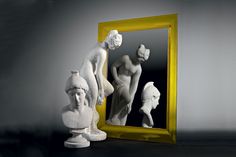 a mirror sitting next to a white sculpture on top of a wooden table in front of a yellow frame