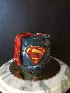 a cake with a superman symbol on it is sitting on a marble plate and has red icing