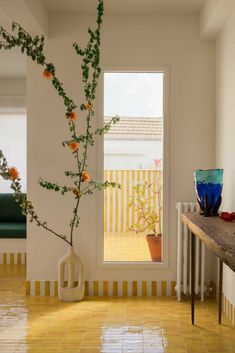 a vase with flowers in it sitting next to a window on a tiled floor near a wooden table