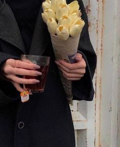 a woman holding a bouquet of tulips in her right hand and a drink in the other