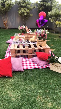 a picnic table set up in the grass with flowers and snacks on it, along with a teddy bear