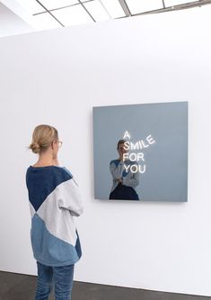 a woman standing in front of a white wall with a smile for you poster on it