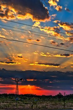 the sun is setting behind power lines and telephone poles with clouds in the sky above