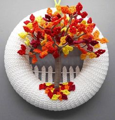 a white plate topped with a tree on top of a wooden fence covered in multicolored crochet