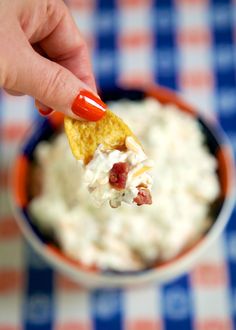 a hand holding a tortilla chip over a bowl of dip