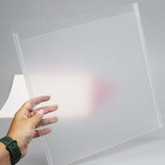 a person holding up a clear plastic sheet on top of a white surface with one hand