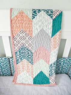 a white bed topped with a quilt next to two blue and orange pillows on top of it