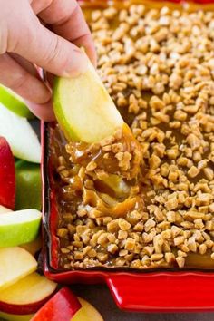 someone dipping an apple into a baked oatmeal in a red baking dish