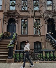 a woman walking down the sidewalk in front of a building with stairs and trees on both sides