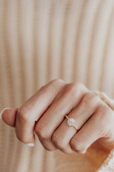 a woman's hand with a diamond ring on her finger, wearing a sweater