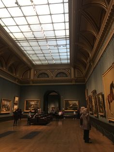 people are looking at paintings on display in an art gallery with skylights above them