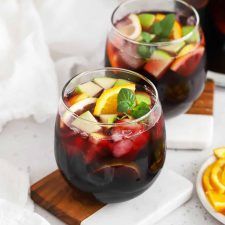 two glasses filled with fruit on top of a wooden cutting board