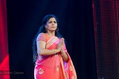 a woman in a pink sari standing on stage with her hands folded up to pray