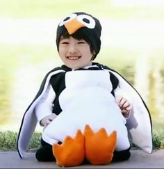 a little boy sitting on the ground with a stuffed penguin in his arms and smiling