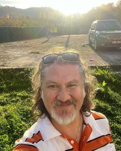 a man with long hair and sunglasses standing in front of a truck on the grass