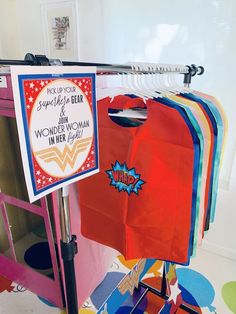 there is a sign that says wonder woman in her light on the clothes rack next to some t - shirts