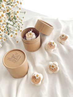 several small candles are in a box on a white sheet next to some daisies