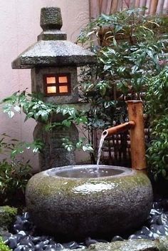 a water fountain in the middle of a small garden with rocks and plants around it