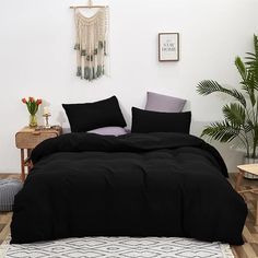 a bed with black sheets and pillows in a room next to a potted plant