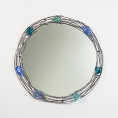 a round mirror with blue and green glass beads hanging on it's sides, against a white wall