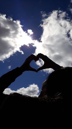 a person making a heart shape with their hands in the air against a cloudy sky