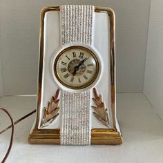 a white clock with gold trim sitting on top of a table