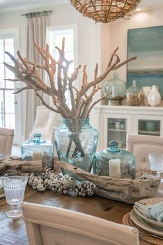 a dining room table is decorated with blue glass vases and driftwood branches in the center