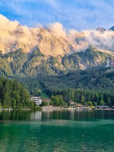 the mountains are covered in clouds and trees near a body of water with houses on it