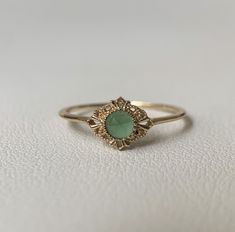 a gold ring with a green stone in the center on a white surface, close up