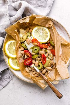 a bowl filled with beans, lemons and other vegetables on top of a table