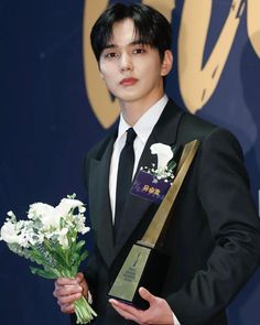 a man in a tuxedo holding a bouquet of flowers and an award plaque