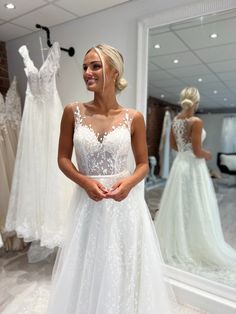 a woman standing in front of a mirror wearing a white wedding dress with lace and appliques