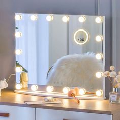 a vanity mirror with lights on it in front of a white dresser and flower vase