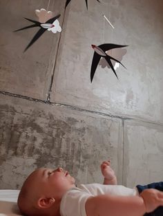 a baby laying on its back in front of a mobile with birds hanging from it