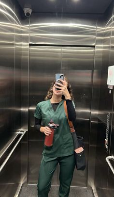 a woman in scrubs taking a selfie with her cell phone while standing in an elevator