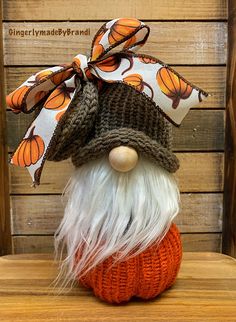 an orange and white knitted pumpkin with a gnome's hat on it sitting on a wooden table