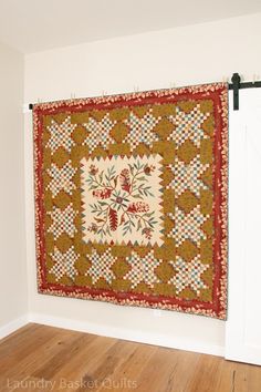 a large quilt hanging on the wall next to a wooden floor in a room with white walls