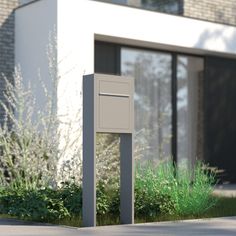 an empty mailbox sitting in front of a building with grass and bushes around it