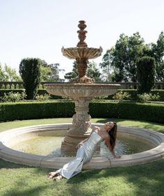 a woman laying on the ground in front of a fountain