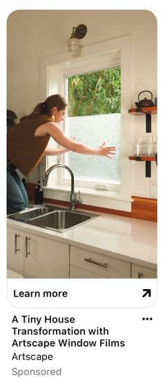 a woman is looking out the window in her kitchen and pointing at something on the counter