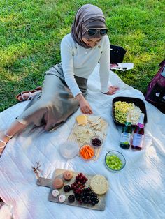 a woman sitting on a blanket with food in front of her and other items around her