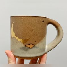 a hand holding a brown and white coffee mug with a bird on it's side