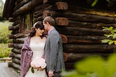 a bride and groom standing in front of a log cabin